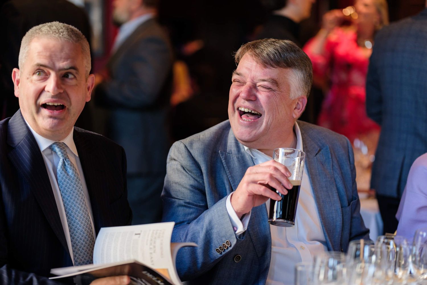 Business professionals laughing and socializing at a formal networking event.