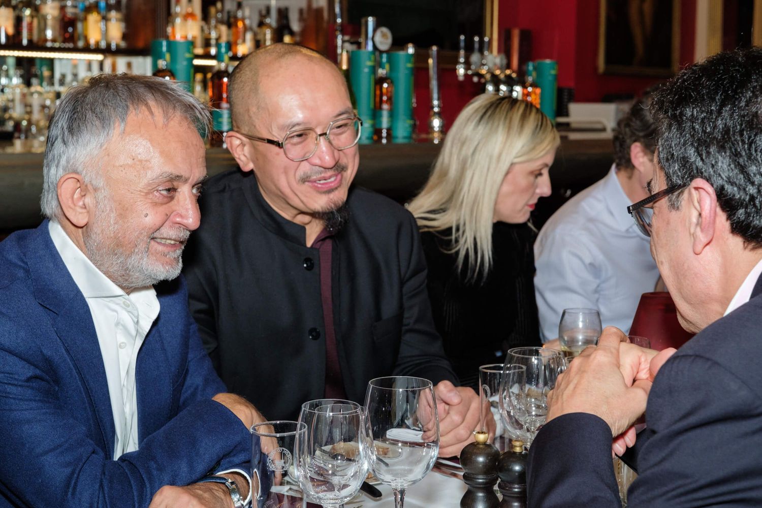 Diners enjoying conversation and wine at an upscale restaurant bar with bottles displayed in the background.