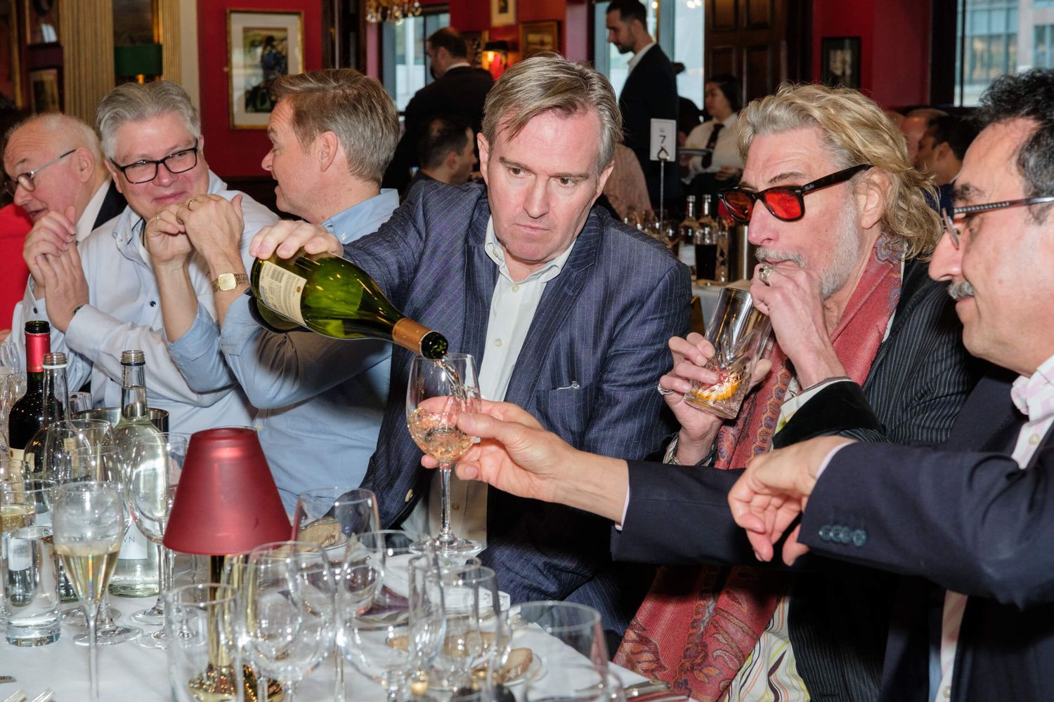 People gathered around tables for a wine tasting event in an elegant restaurant setting with red walls.