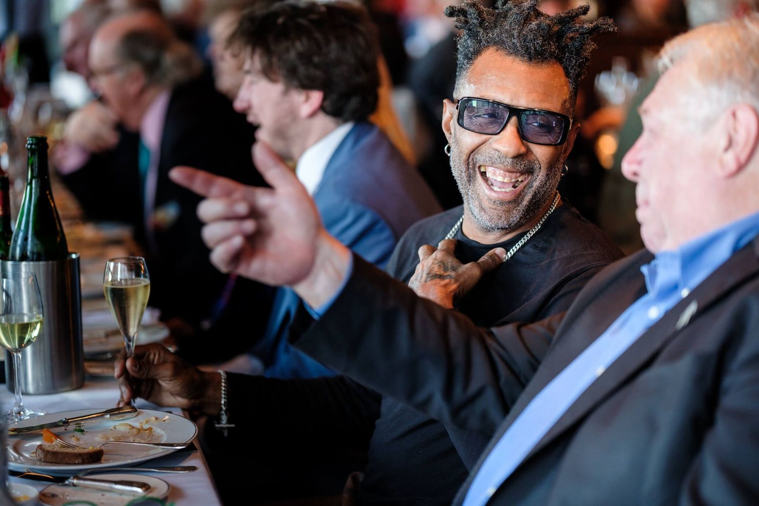 People in business attire share a laugh while dining at a restaurant table.
