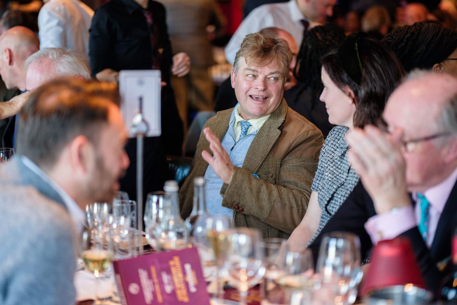 A group of people enjoying drinks and conversation at a crowded social gathering or reception event.