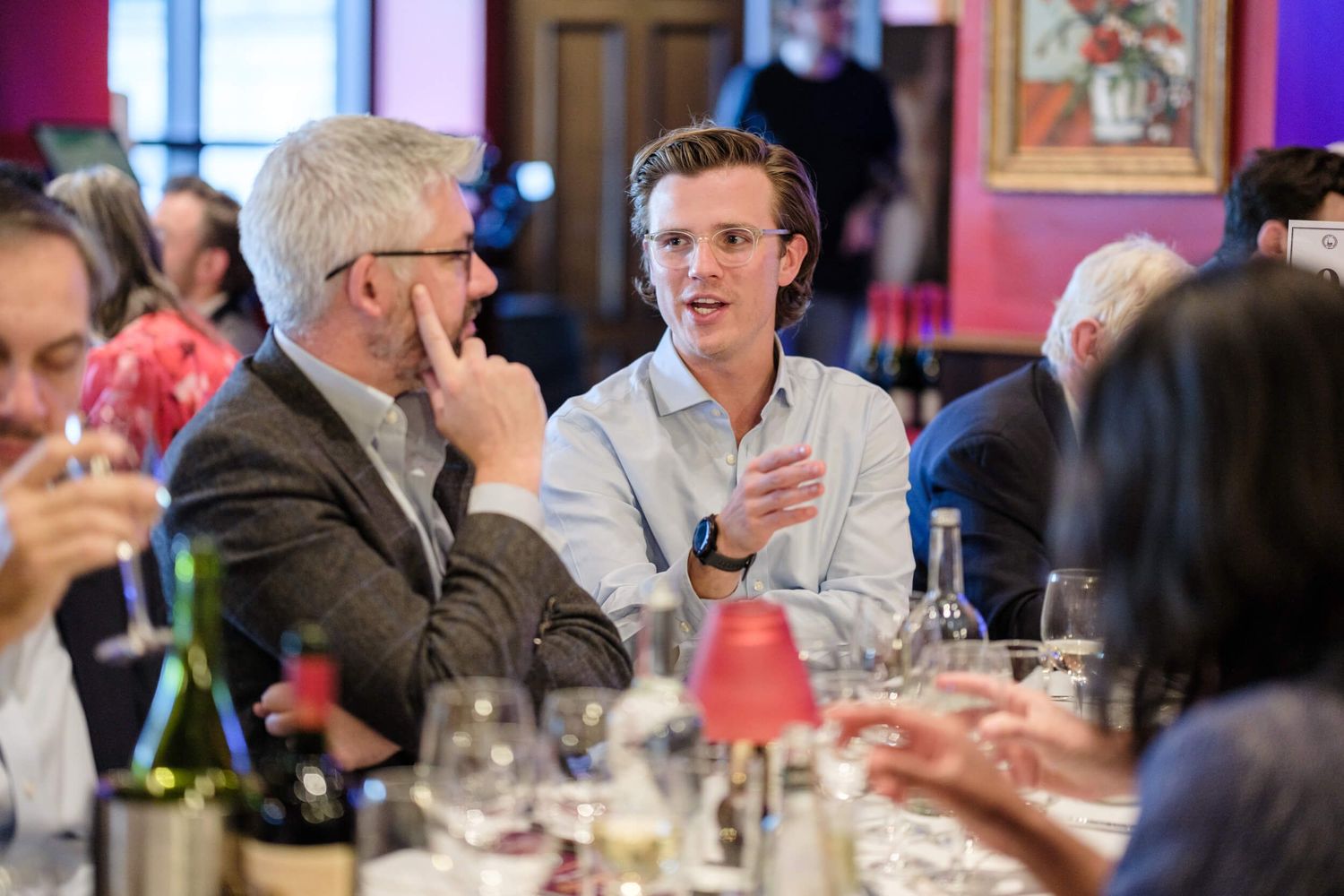 Guests engage in lively conversation around tables at an upscale restaurant dinner event.