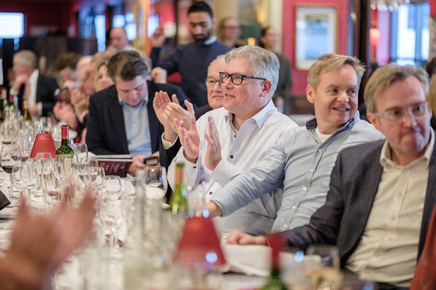 Business professionals seated at tables during a corporate event with drinks and networking in a well-lit venue.