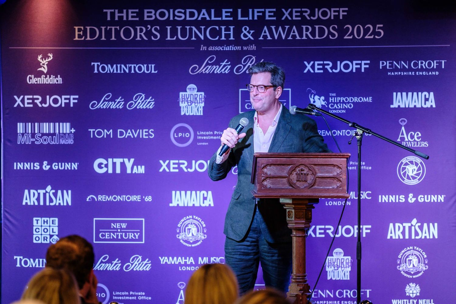 Event attendees pose with awards in front of a purple branded backdrop with sponsor logos at an industry ceremony.