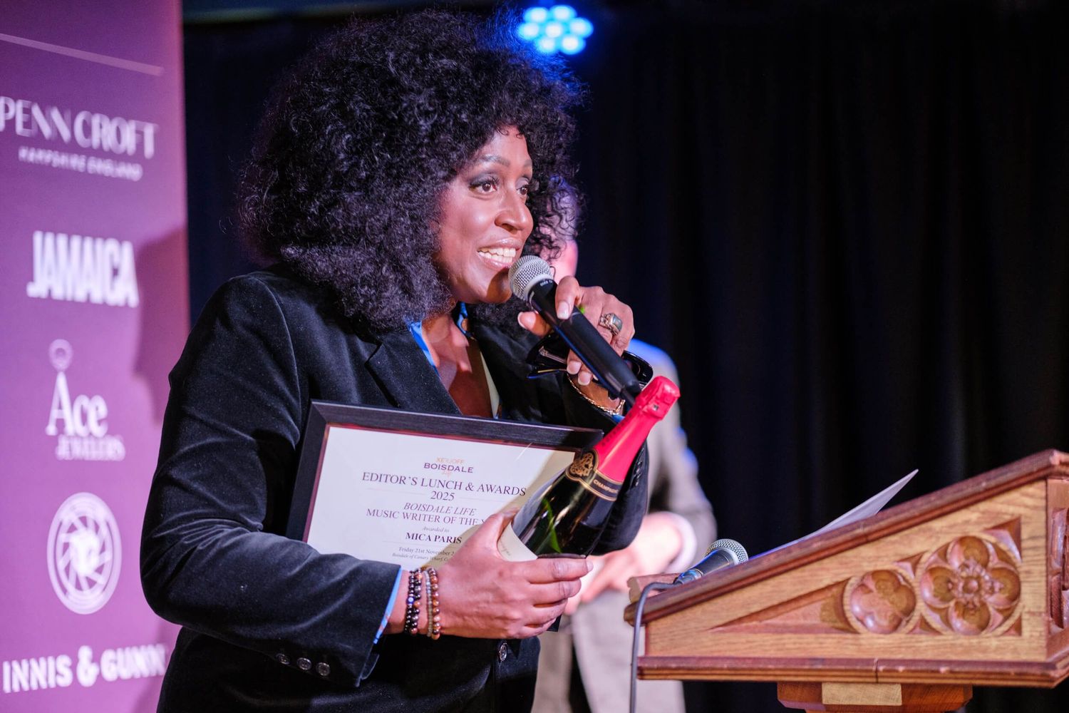 Awards ceremony speakers present at wooden podiums on stage with purple lighting and banners.