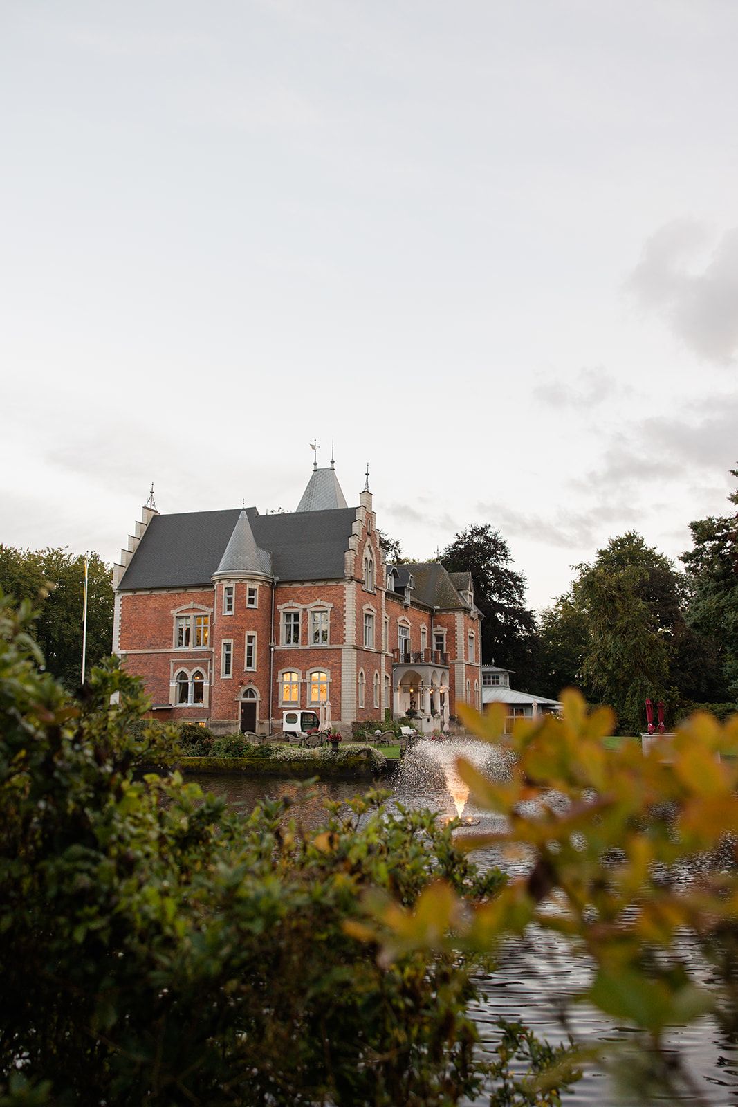 Scenic view of a historic red brick mansion with Victorian architecture set against an autumn sky and foliage.
