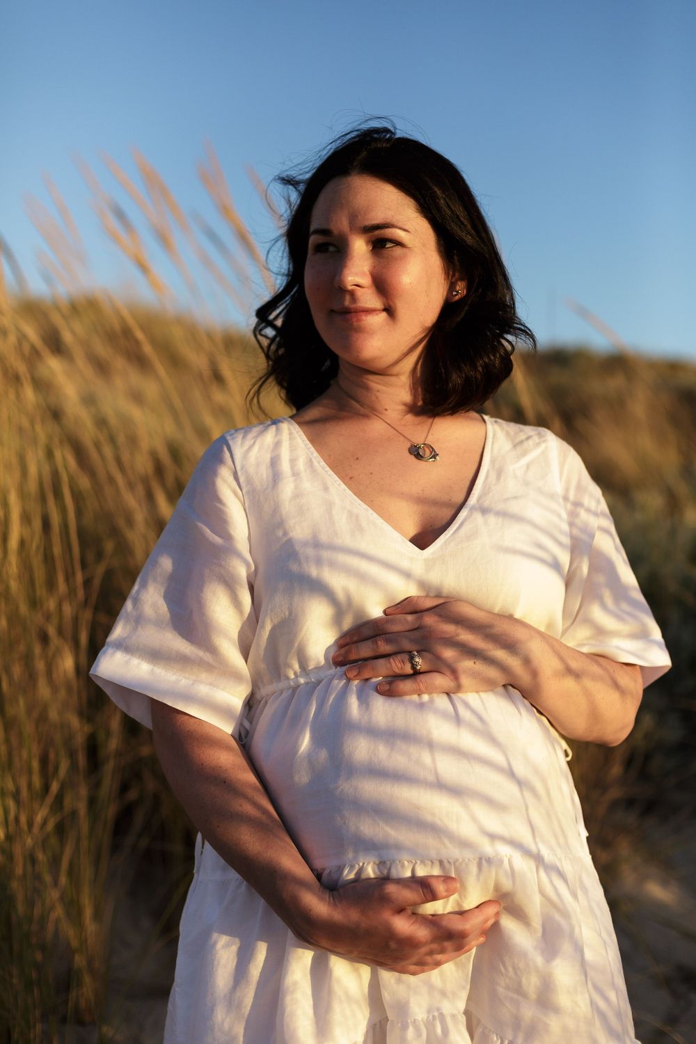 A pregnant woman holding her bump in golden lighting during an outdoor maternity photoshoot in Perth