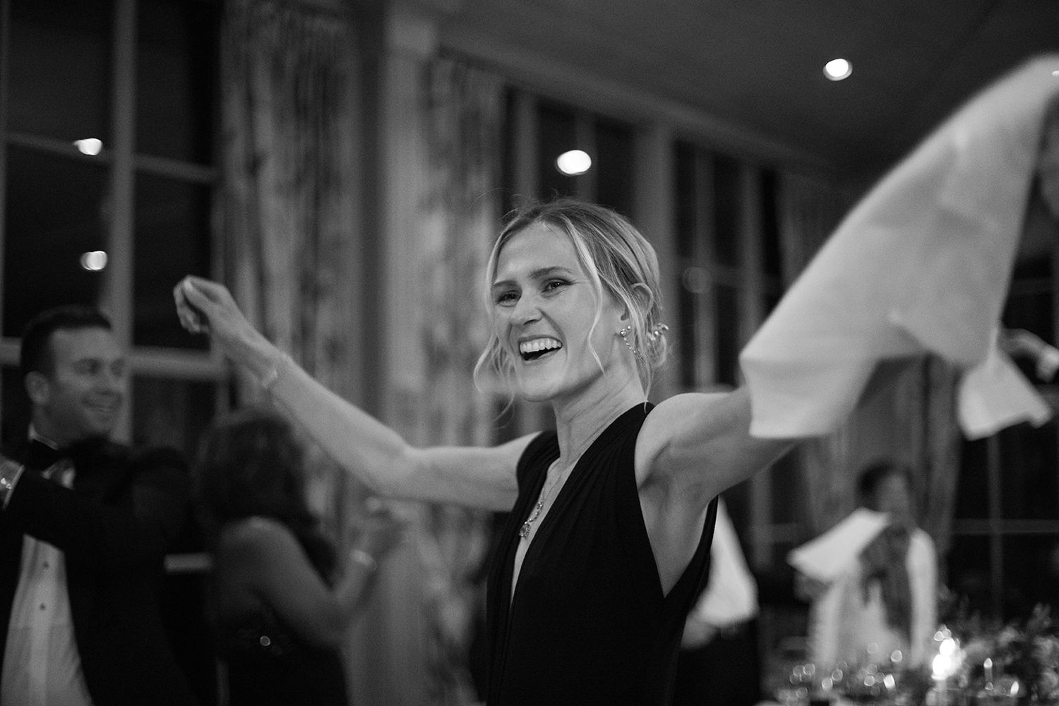 A black and white wedding reception scene with people dancing and waving napkins in celebration.