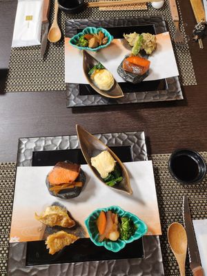 Multiple plates of Japanese cuisine arranged on a dark wooden table with decorative placemats.