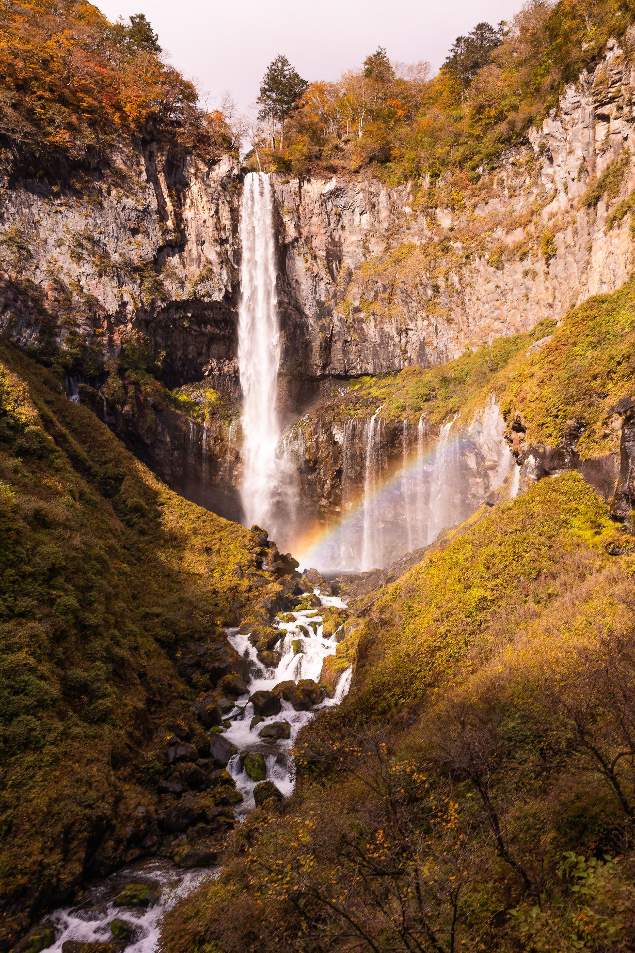Majestic Kegon Falls cascades down rocky cliffs surrounded by autumn foliage in Nikko National Park, Japan.