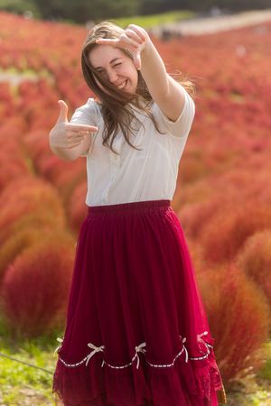 A person wearing a white top and burgundy tulle skirt twirls in front of vibrant red autumn foliage.
