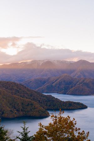 Scenic mountain lake view at sunset with snow-capped peaks and autumn foliage in the foreground.