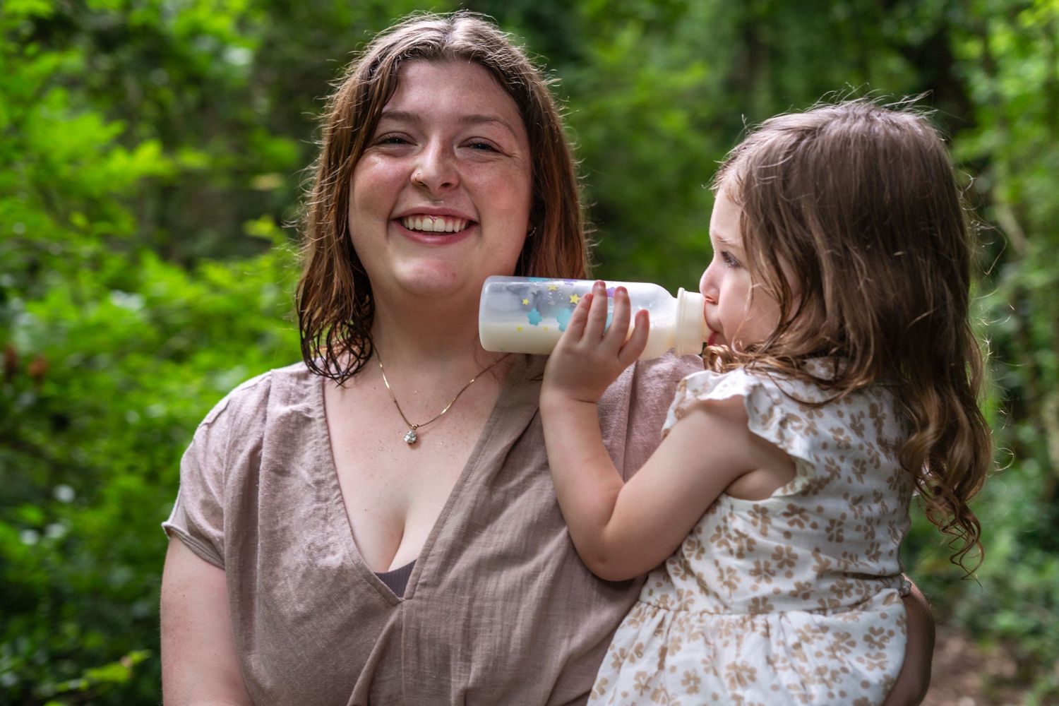 A parent and child share a joyful moment together while sitting outdoors in a lush green forest setting.
