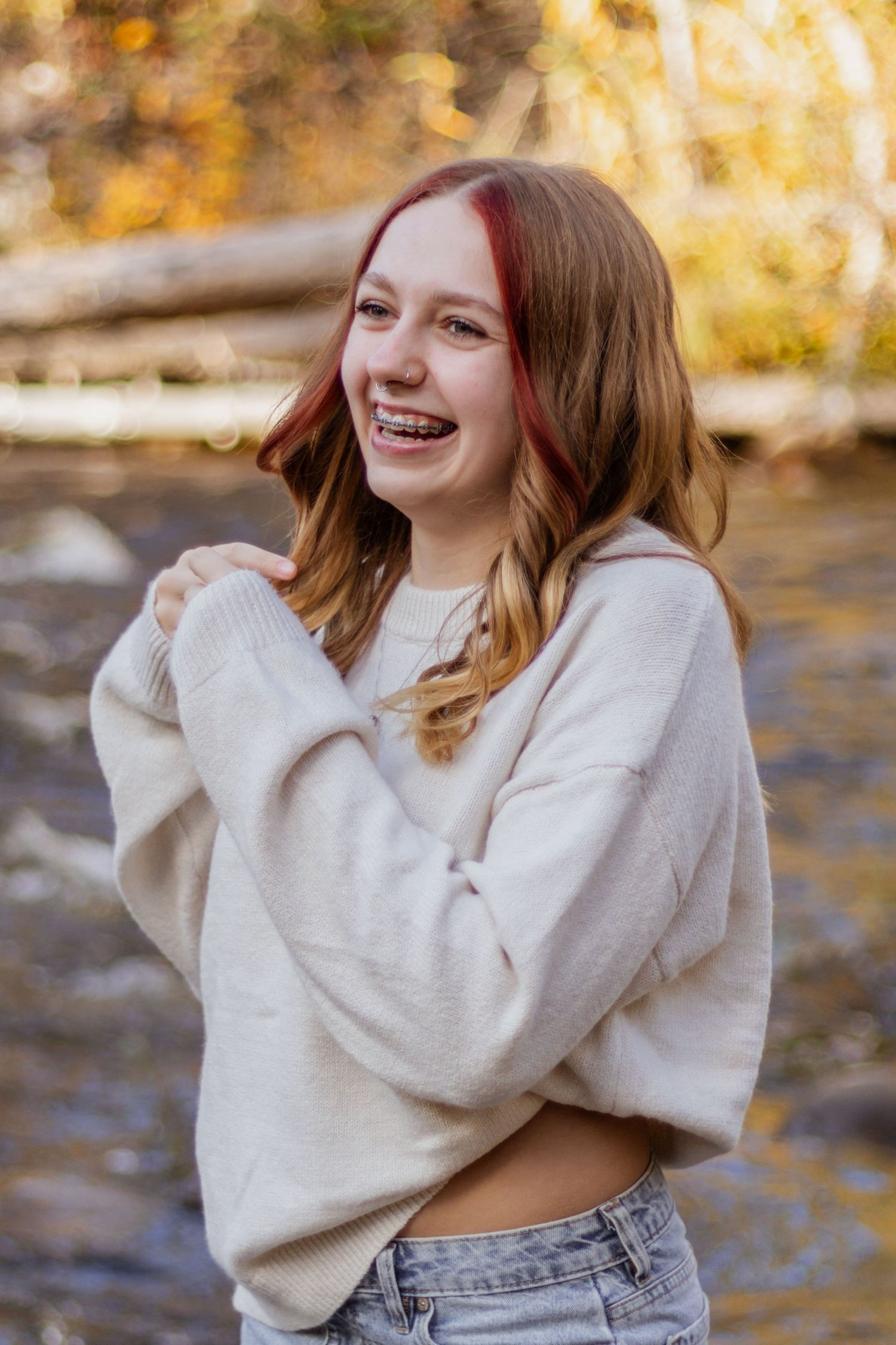 Smiling teenage girl with red highlights laughing by a creek in autumn.
