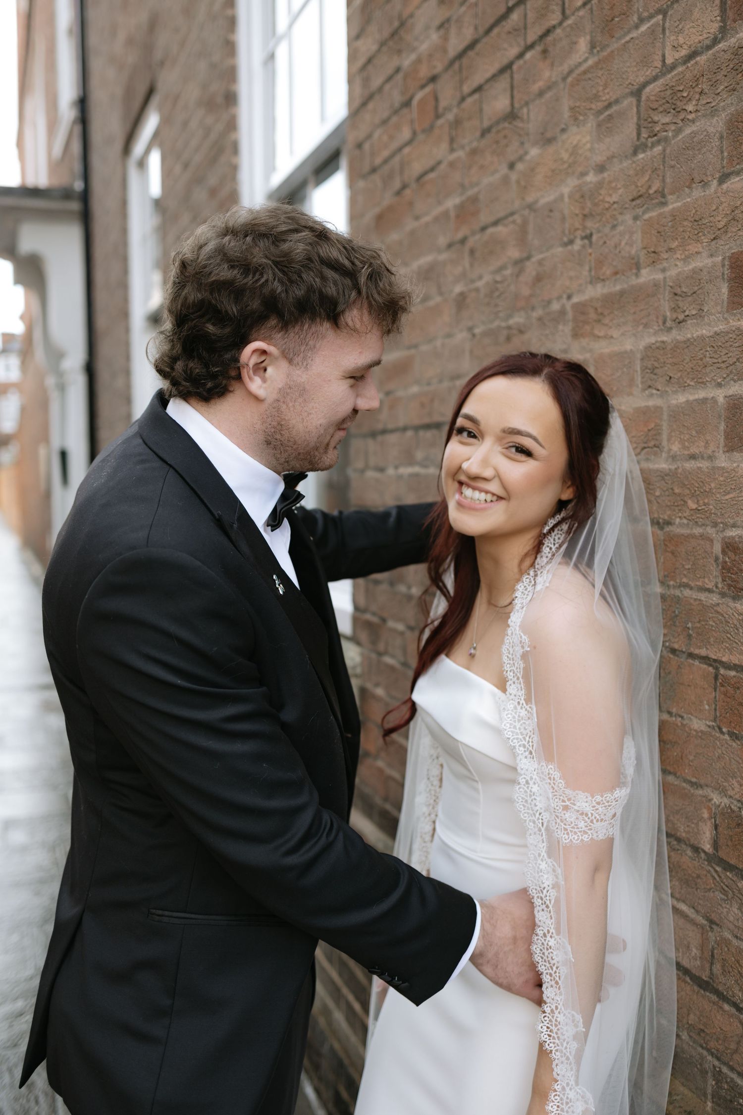 A romantic wedding couple shares tender moments against a brick wall in a series of candid shots.