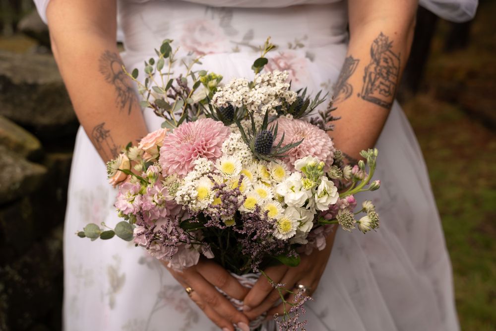 Close-up view of hands holding a delicate pastel pink and white wildflower bouquet with greenery accents.