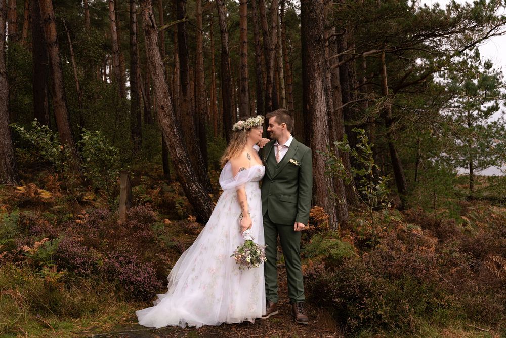 A couple in wedding attire shares an intimate moment in a scenic pine forest setting.