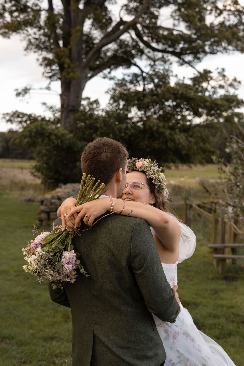 A couple embraces in a romantic moment outdoors with trees and greenery in the background.