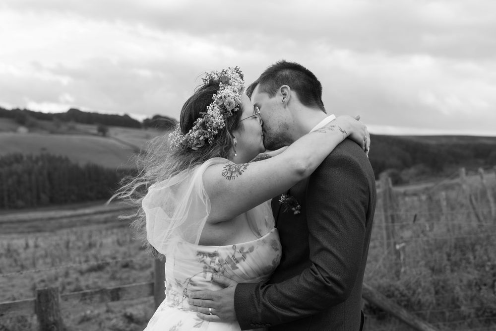 A romantic couple embraces in a field against a scenic mountain landscape backdrop during a wedding photo session.