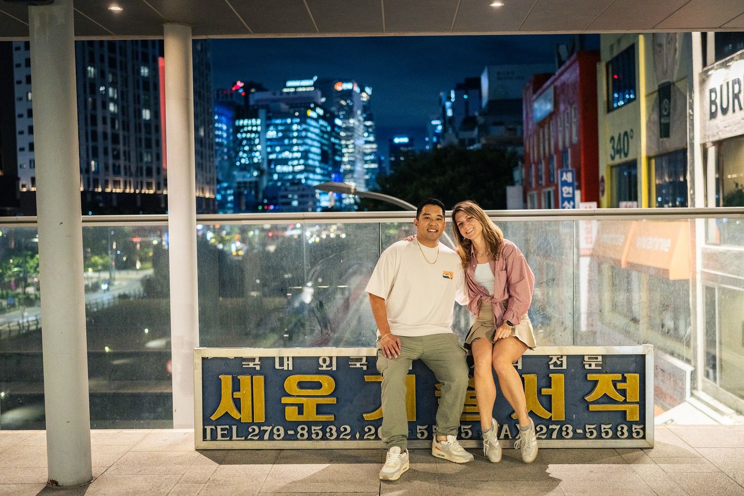Panoramic view of a modern urban train station platform in South Korea with Korean signage and illuminated city backdrop.