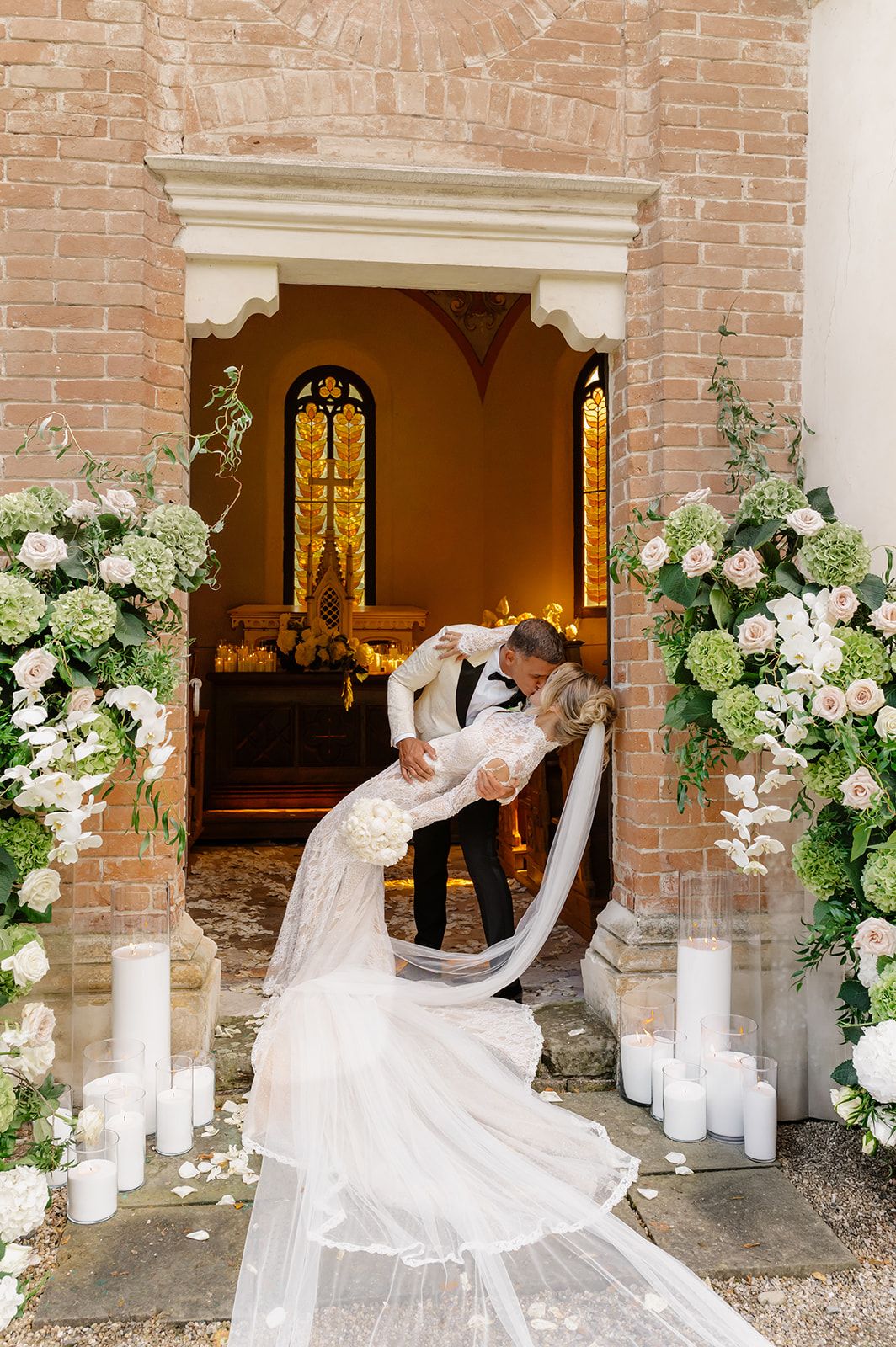 Romantic wedding portraits with flowing veil against brick archways decorated with white flowers.