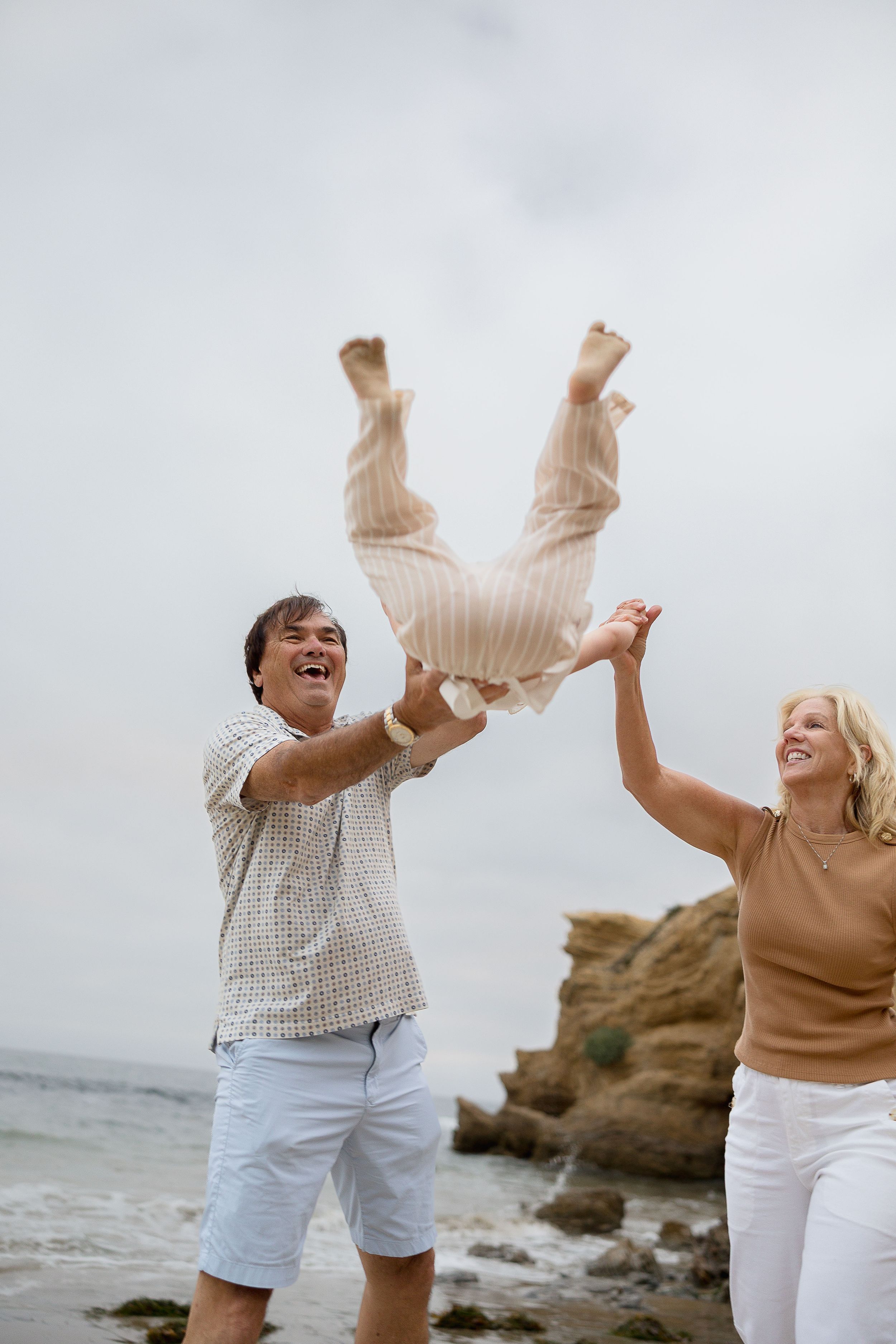 Candid beach family photos at Crystal Cove with grandparents holding their grandchild