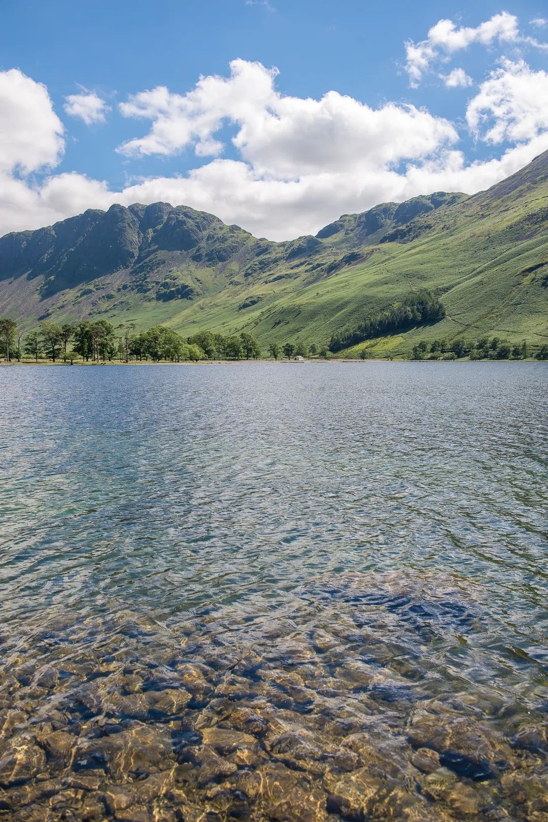 Crystal clear lake water with mountains and clouds in the distance.