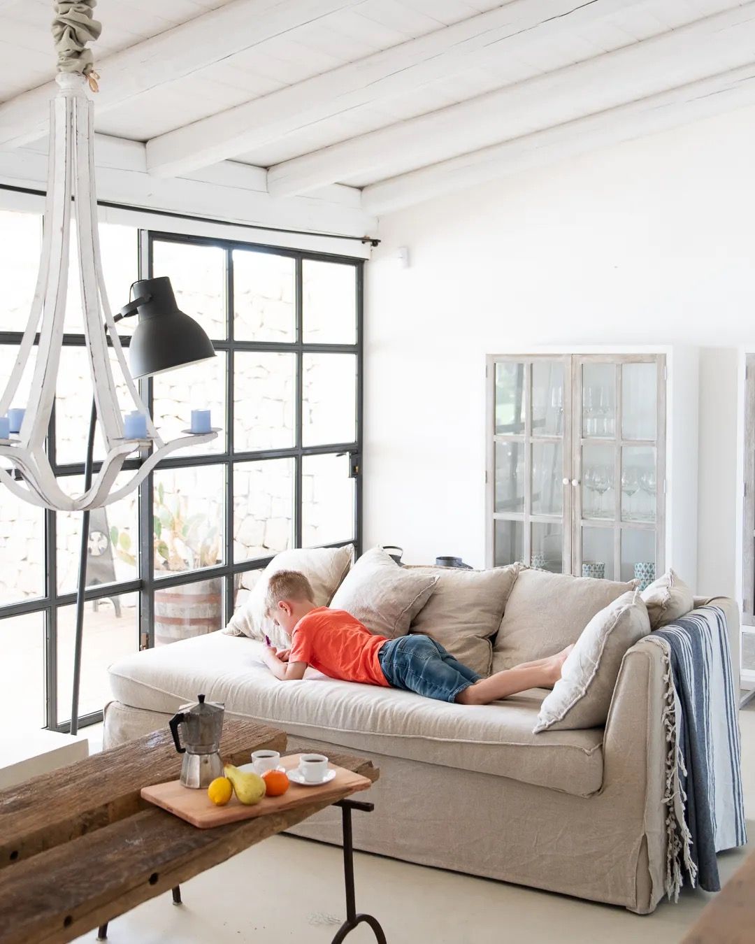 A cozy living room with a light sofa, large industrial-style windows, and bright natural light filling the space