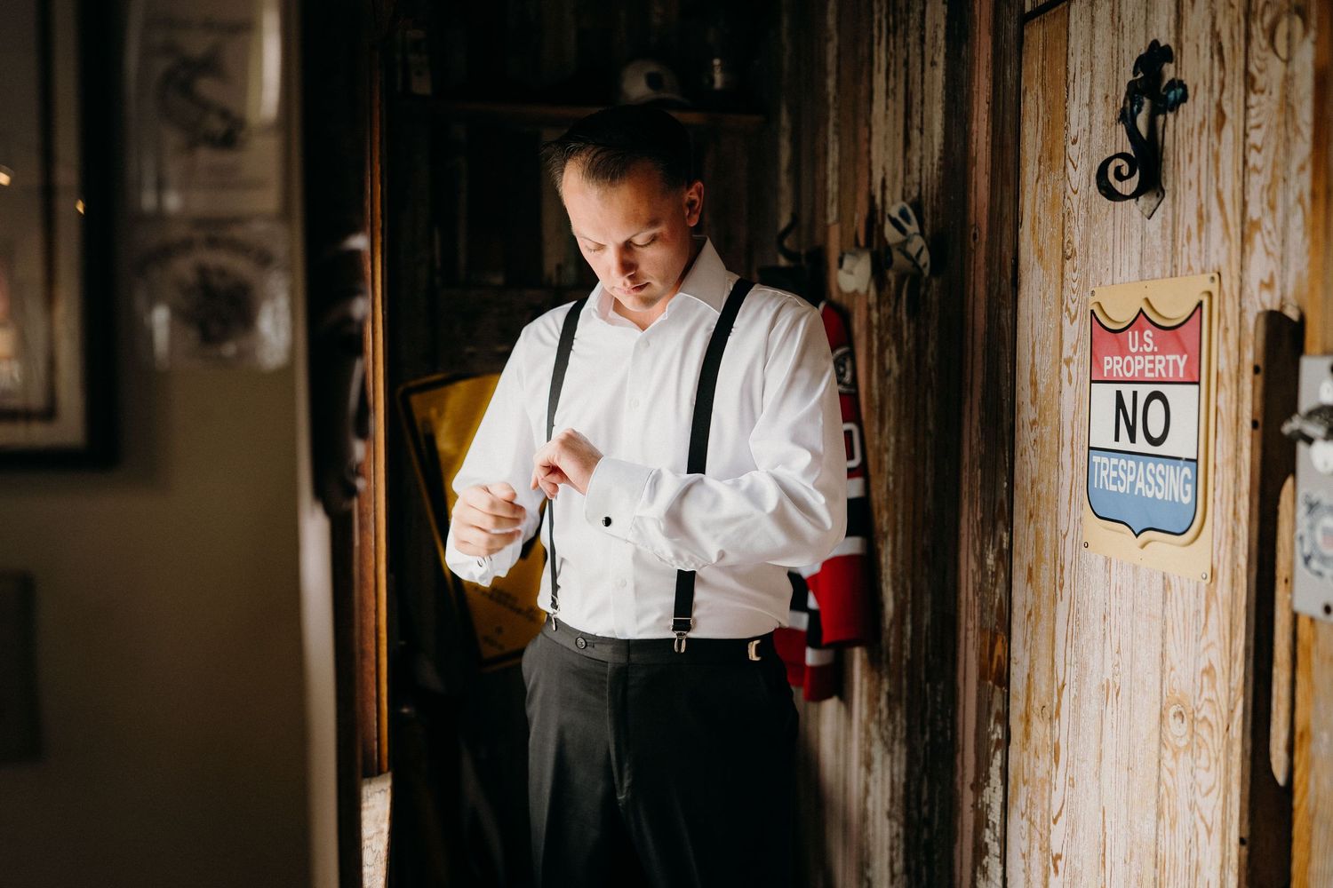 A person in a white dress shirt and suspenders stands in a dimly lit rustic wooden hallway.