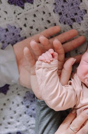 Tiny newborn baby feet and hands resting on purple knitted blanket.