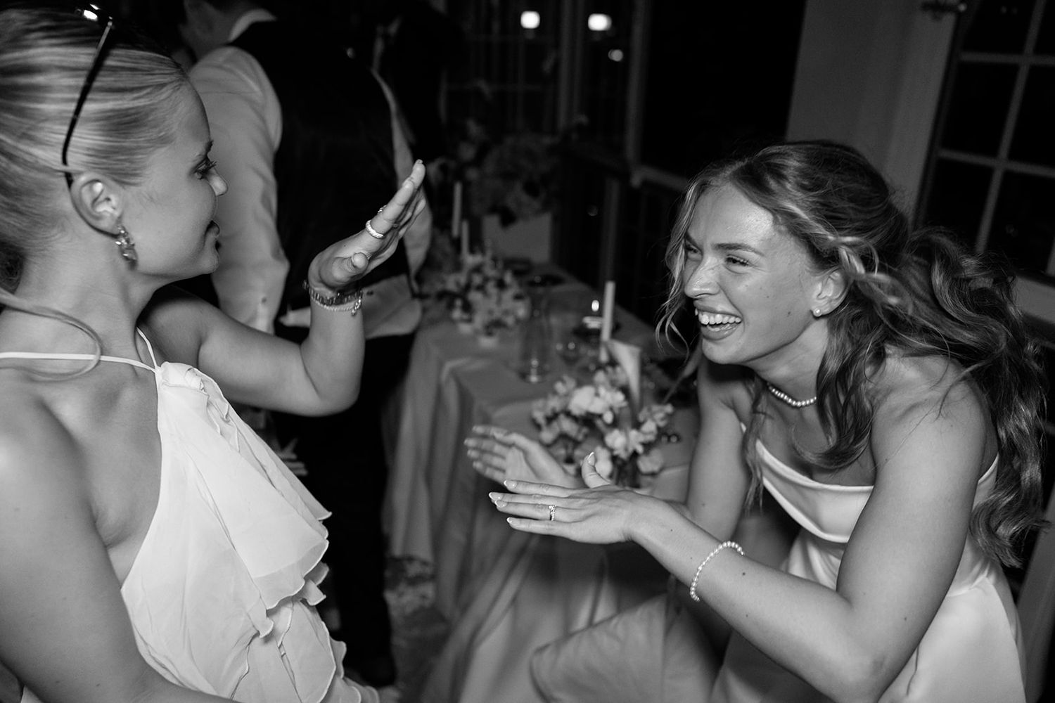 A candid black and white photo of two people laughing and sharing a joyful moment at a wedding reception.