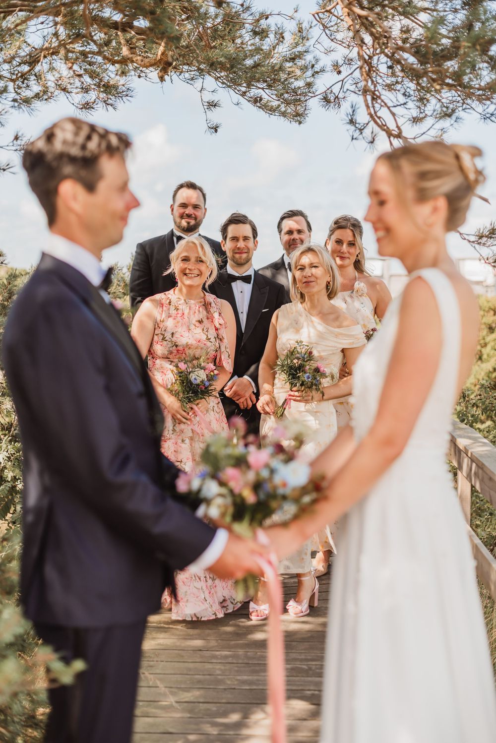 Wedding party gathers on stone steps under pine trees during an outdoor summer ceremony.