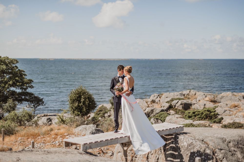 A couple shares a romantic moment on a rocky coastal cliff overlooking the ocean during a wedding photoshoot.