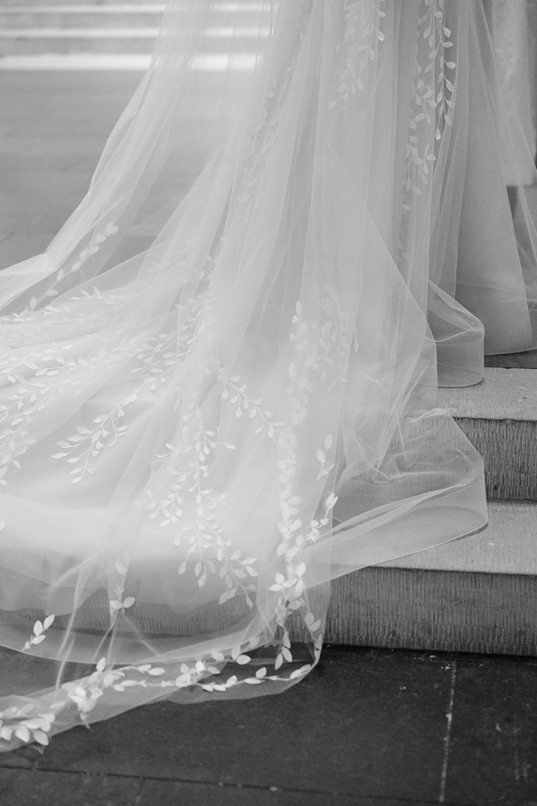 Delicate white tulle wedding dress train with embroidered floral details sweeps across a dark floor.