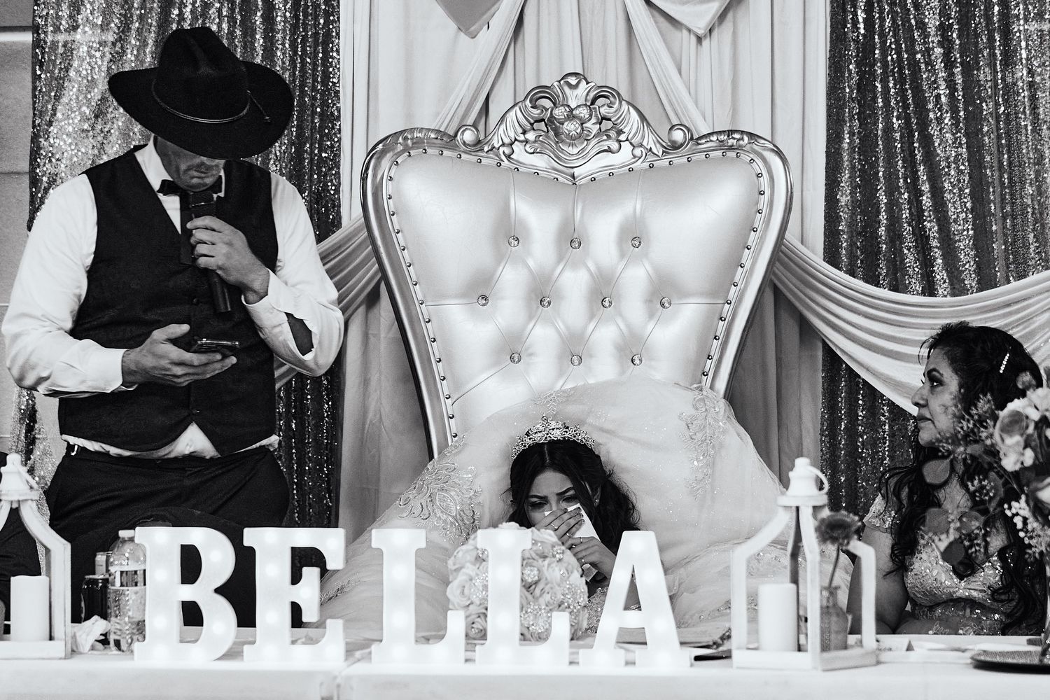 Black and white wedding reception photo showing an ornate white throne chair and decorative letters spelling BELLA.