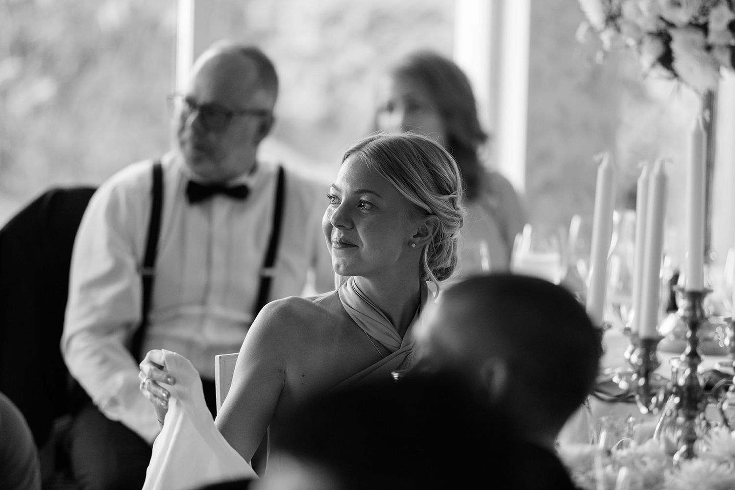 Black and white candid photograph at an elegant dinner event with formal attire and candlelit table settings.