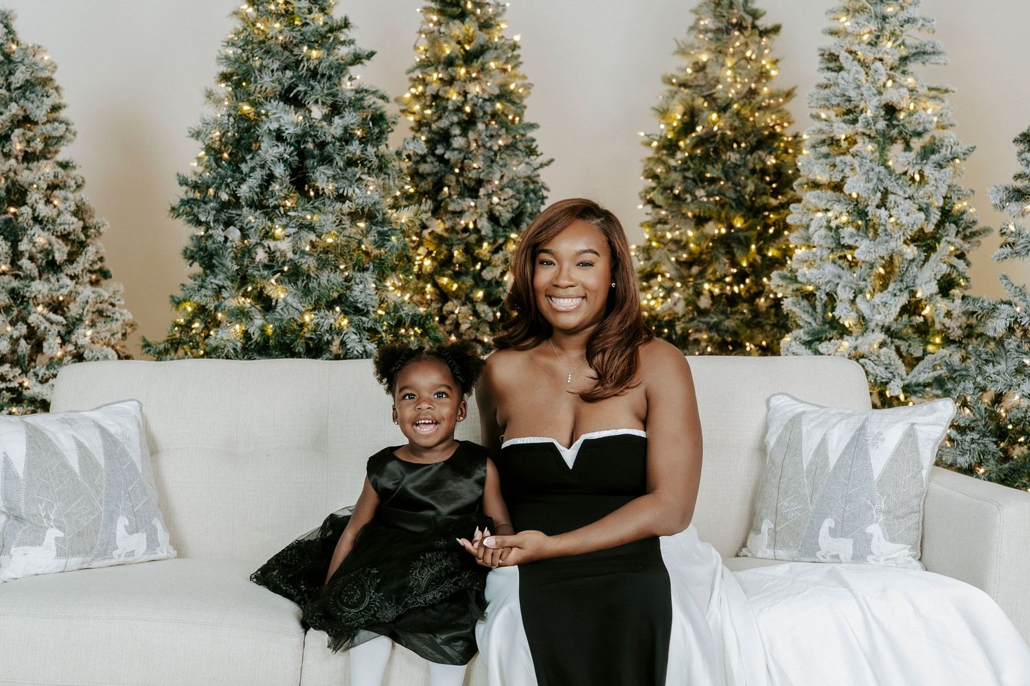 Elegant holiday portrait with illuminated Christmas trees and white decor in the background.