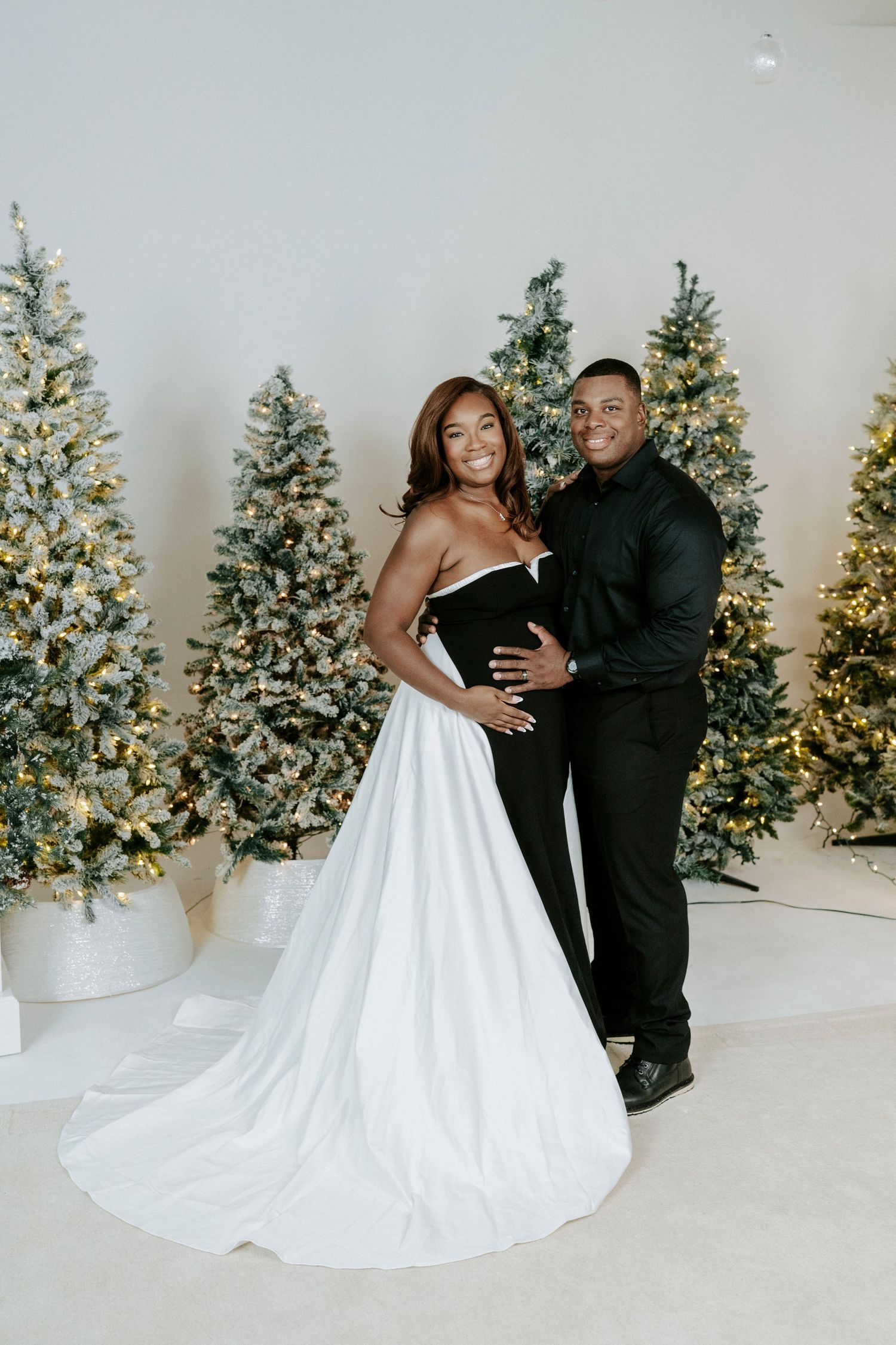 A couple embraces in front of decorated Christmas trees during a winter wedding photo session.