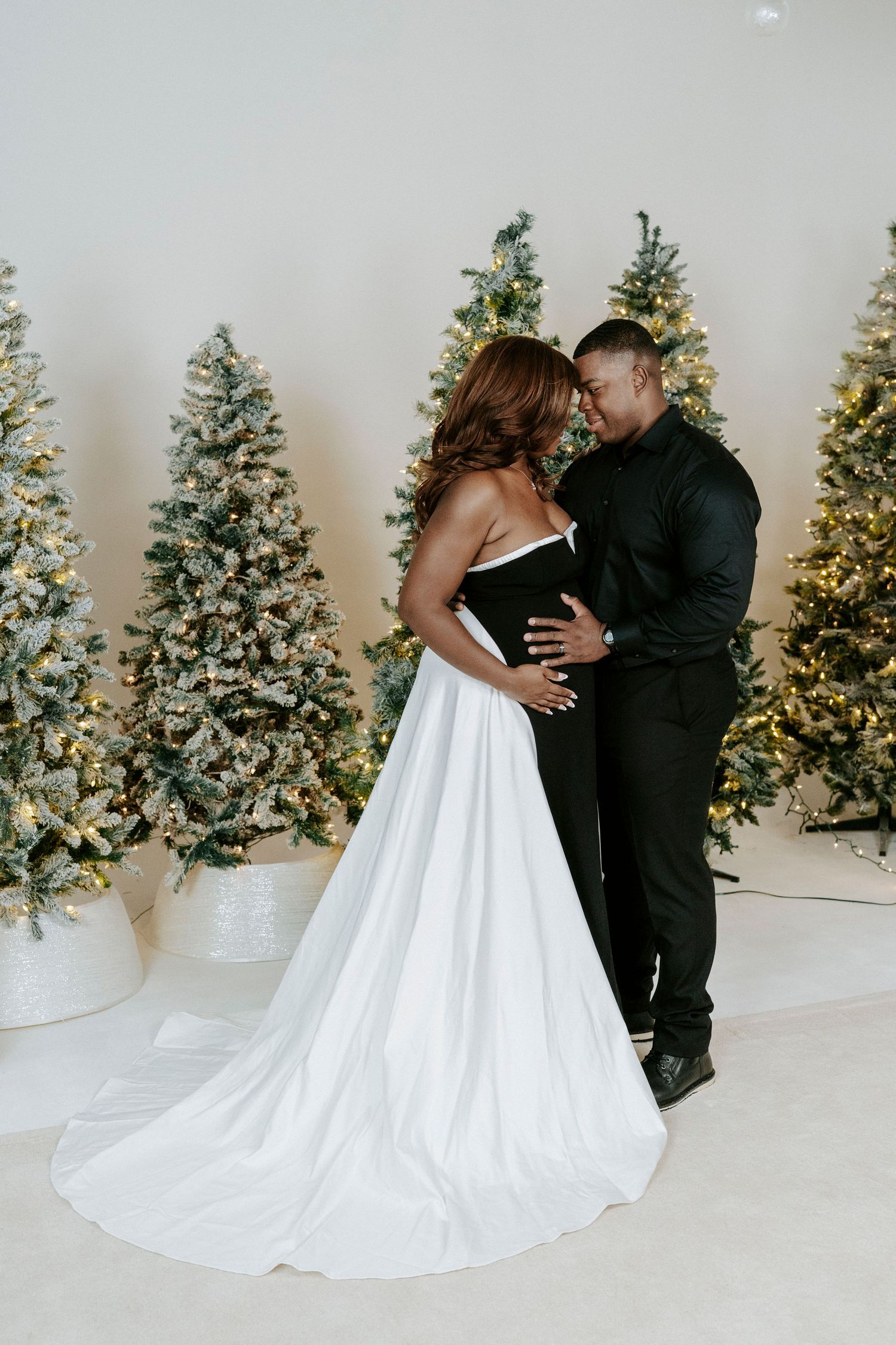 A couple shares an intimate moment in front of lit Christmas trees during a winter wedding photoshoot.