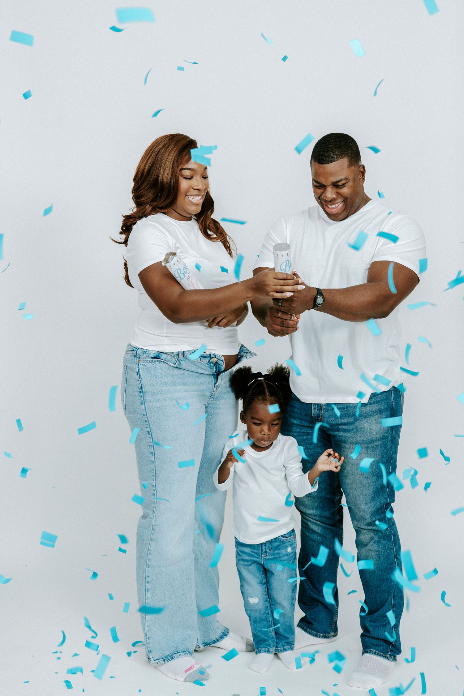 A family wearing matching white shirts and jeans poses together as blue confetti falls around them during a photo shoot.