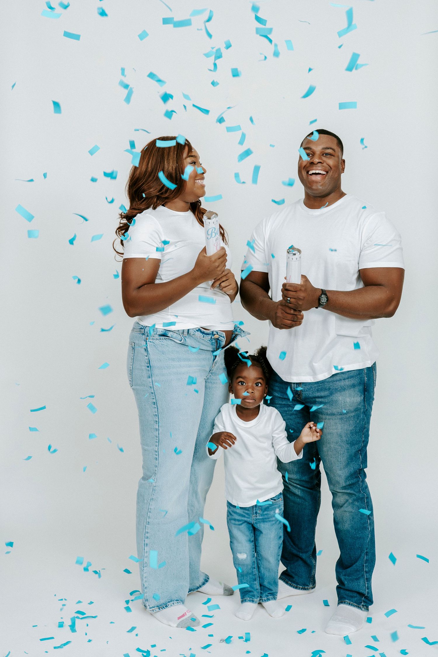 A joyful family celebration with blue confetti falling in a bright white studio setting.
