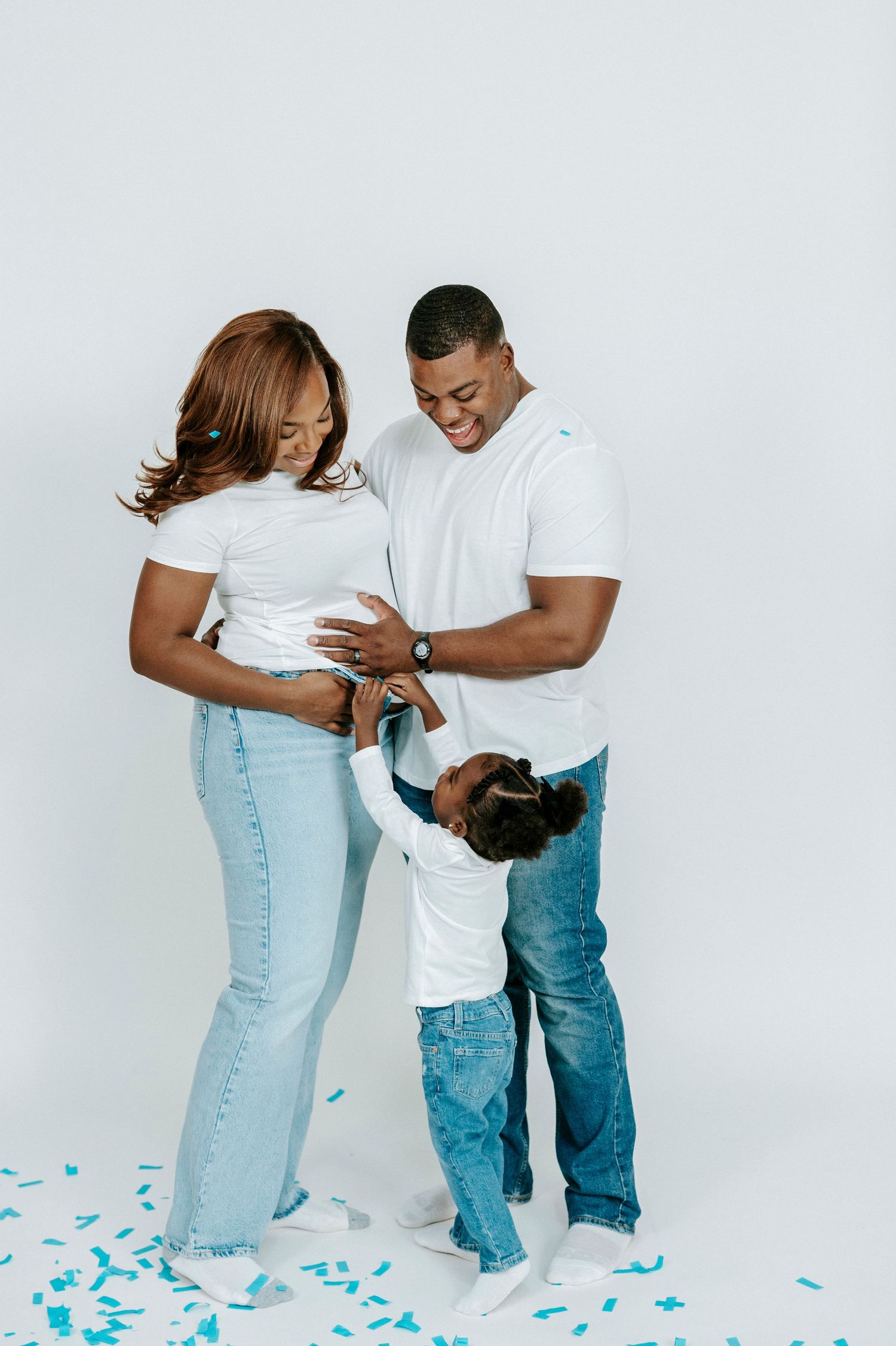 A family celebrates with confetti during a gender reveal photo shoot against a white backdrop.