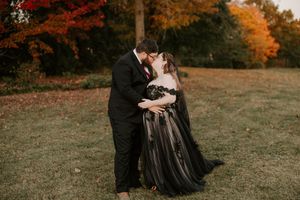 A romantic couple's photoshoot in black attire against autumn trees.