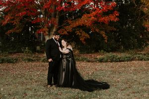 A romantic couple in formal attire embraces under vibrant red autumn maple trees.