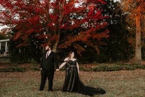 A couple in formal black attire poses against a backdrop of vivid fall colors.