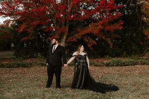 A playful moment between a couple in formal wear beneath autumn trees.