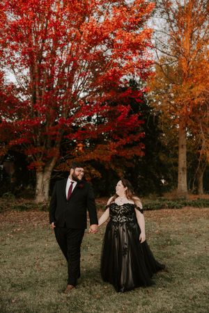 Elegant couple poses for photos on grassy hill surrounded by bright red and orange fall foliage.