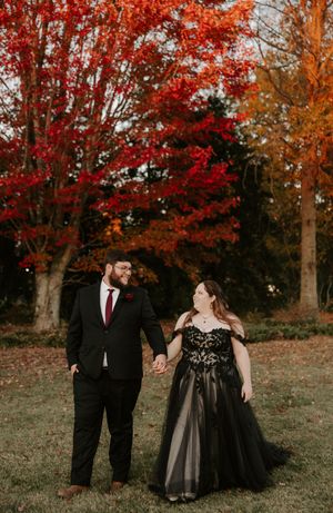 Couple shares a tender moment while walking through a scenic autumn landscape with red maple trees.