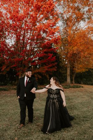Dancing couple in formal wear enjoys their photoshoot surrounded by fall foliage.