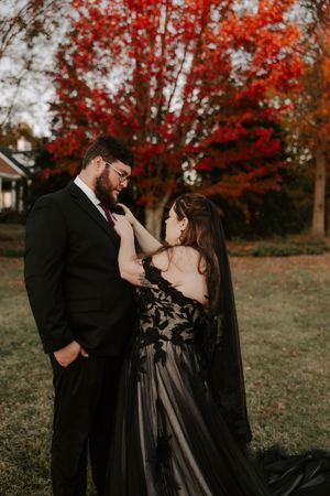 Intimate moment between couple in formal wear during autumn photoshoot with red maple trees.